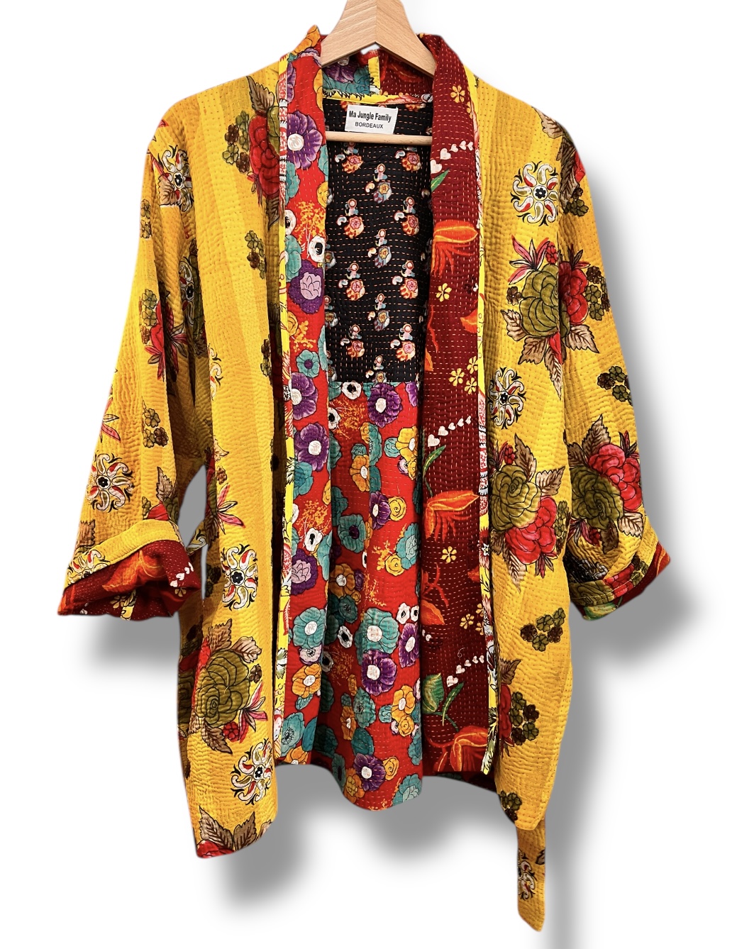 Veste kantha vintage réversible en coton recyclé, faite main à partir de saris indiens – pièce unique aux motifs fleuris colorés, exposée sur un portant. Rouge, vert, fleurs, orange, reversilble