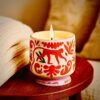 Bougie artisanale Monkey en céramique peinte à la main, motif singe rouge orangé, posée sur une table en bois avec une couverture en laine beige pour une ambiance cocooning et chaleureuse. Boîte décoration, adopo, paddywax, jungle